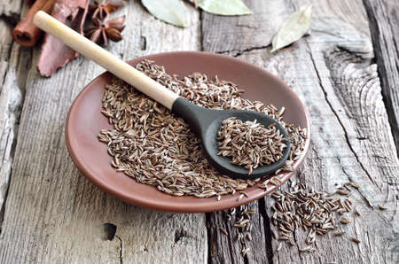 Cumin seeds in a brown plate on a rustic wooden background