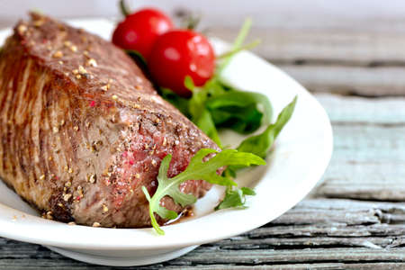 Roasted meat on a white dish decorated with fresh arugula leavesの写真素材