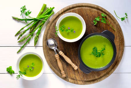 Green spring pureed asparagus soup served in plates decorated with various garden herbs