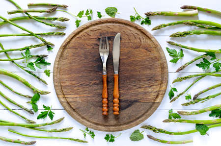 Clean eating or healthy foods concept background, fresh green asparagus and various herbs around white vintage plate, top viewの写真素材