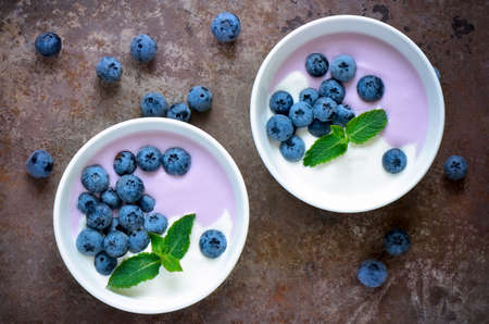 Light greek yogurt or cream dessert with fresh blueberries served in two white bowls; top view; stylized photoの写真素材