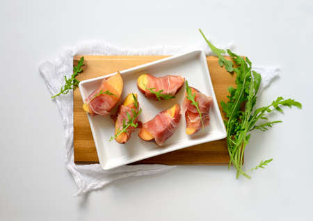 Peach slices wrapped in prosciuto decorated with arugula fresh leaves, fast and simple party snack, top viewの写真素材