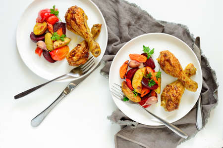 Chicken drumsticks with roasted vegetables garnish in two plates, view from above
