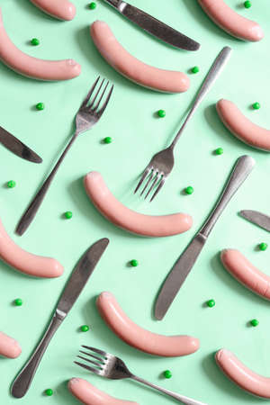 Sausages, forks and knives and green peas, flat lay, view from above, food concept, stylized photoの写真素材