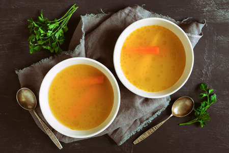 Bouillon or broth served in two bowls on a rustic dark table, view from aboveの写真素材
