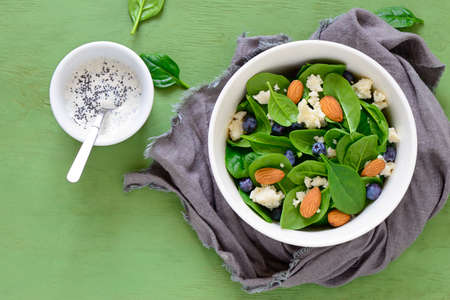 Spinach, almond and goat cheese salad served in a bowl with yogurt and poppy seed dressing in a cup, view from aboveの写真素材