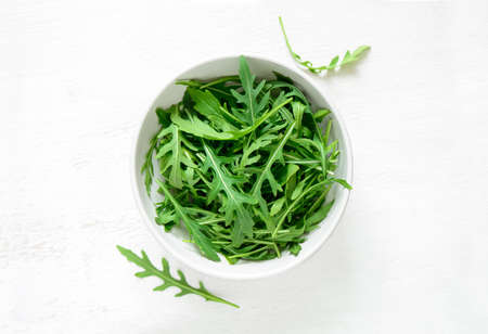Fresh arugula leaves in a white bowl, top viewの写真素材