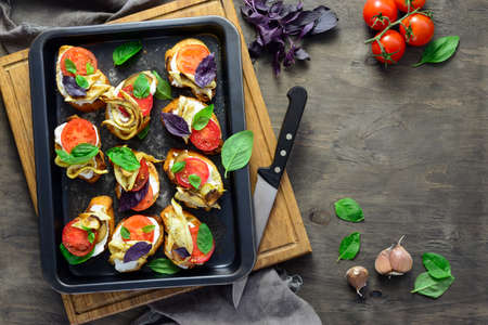 Spicy canapes with baked zucchini, tomatoes and soft cheese seasoned with fresh basil leaves and garlic, view from above, flat lay, space for a textの写真素材
