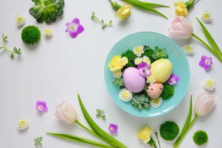 Easter greeting floral background with a space for a text, decorative arrangement with pastel colored hand painted eggs and spring flowers, view from above, flat layの写真素材