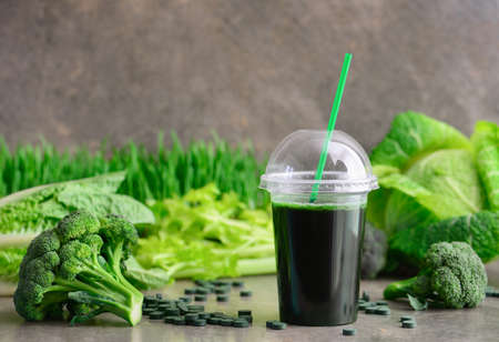 Detox green smoothies concept, a glass of green diet detox drink and various fresh green vegetables such as broccoli and spirulina pills behind, front viewの写真素材