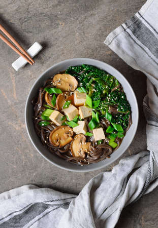 Diet vegetarian bowl of soba noodle soup rich with various sources of vegan protein such as mushrooms, tofu and kale; the meal seasoned with sesame seeds and chives. View from above arrangement.の写真素材