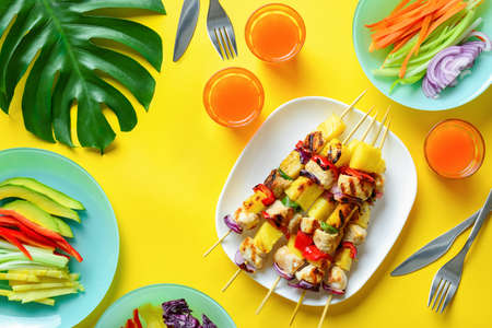 Summer simple recipe for grilling, hawaiian chicken kabobs served with freshly diced vegetables and some orange drink in glasses, view from above の写真素材