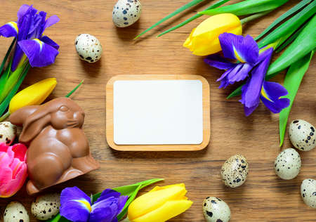 Easter background with a traditional treat chocolate bunny and spring flowers on wooden background, view from above, space for a textの写真素材