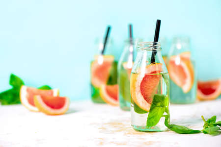 Pink grapefruit and fresh basil infused drink  in bottles, spa fruit water, or summer party alcoholic jin tonic cocktail served in small shots, front view, space for a textの写真素材