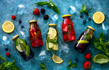 Fruits and berries and aromatic herbs spa infused waters in glass bottles, flat lay composition