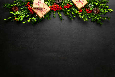 Noel or Christmas dark background with gift boxes and natural winter holidays traditional botany decor such as red berries and evergreen branches arranged in a header, flat lay composition with copy space for a greeting textの写真素材