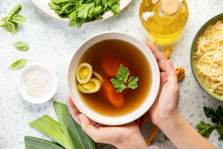 Basic bone broth in a bowl held by hands view from aboveの写真素材
