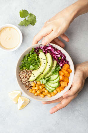 Vegan Buddha bowl with roasted chickpeas and tahini sauce, top down view of hands serving the bowlの写真素材