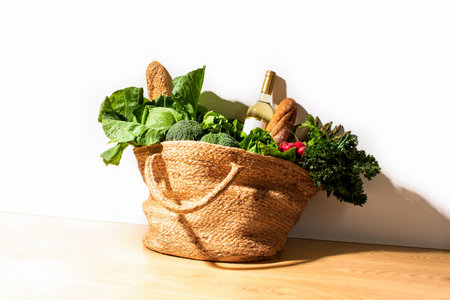 Shopping straw bag full of fresh leafy vegetables and a bottle of white wine. Strong sunny shadow....