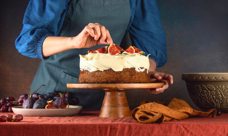 Woman is decorating fall pumpkin spice sponge cake with figs on buttercream toppingの写真素材