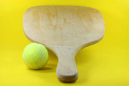 beach wooden racket with yellow ball in yellow backgroundの写真素材