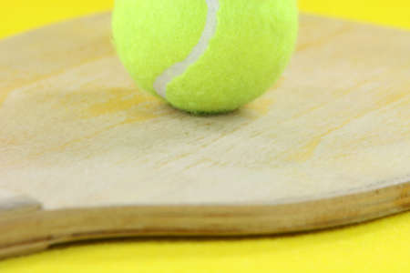 beach wooden racket with yellow ball detail in yellow backgroundの写真素材