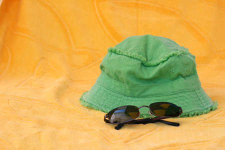 summer accessories green hat and black sunclasses on yellow towelの写真素材