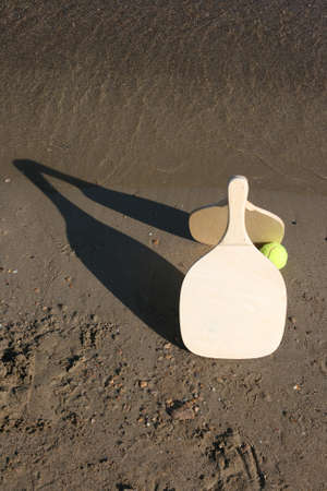 two wooden beach rackets by the shore with yellow ballの写真素材