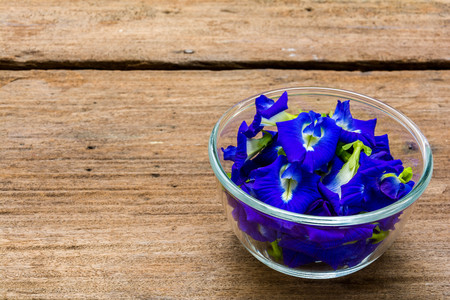 Pea flowers placed in a glass bowl on a wooden tableの写真素材