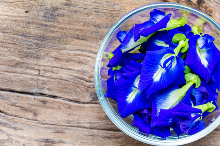 Pea flowers placed in a glass bowl on a wooden tableの写真素材