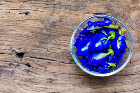 Pea flowers placed in a glass bowl on a wooden tableの写真素材