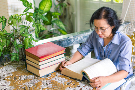 Middle-aged woman reading a book at home during the dayの写真素材