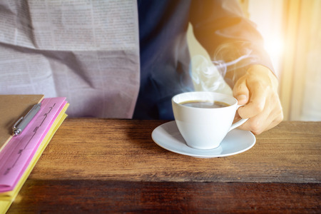 Male businessmen read newspapers and drank black coffee early in the morning at the desk. With pink and yellow filesの写真素材