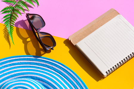 Blue hat and sunglasses on colorful paper with notebook travel and fashion styleの写真素材