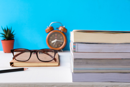 Books and glasses on a white wooden table are clocks and decorations With a room with a sweet and quiet blue wall.selective focusの写真素材