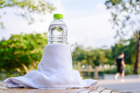 Plastic water bottle and white cloth on desk with running exercise people at the park.の写真素材