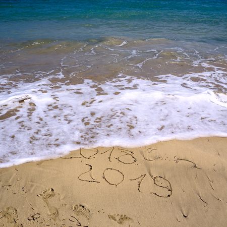 New Year 2019 is coming concept - inscription 2018 and 2019 on a beach sand, the wave is starting to cover the digits 2018. Copy space, flat lay, top view,  square,の写真素材