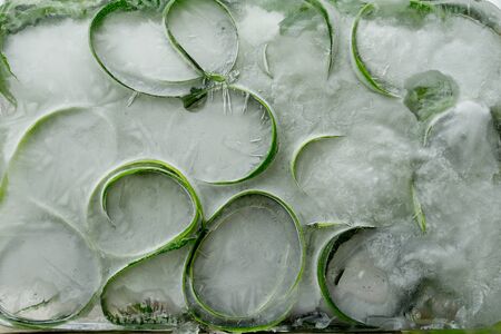 Background  skin and piece of  fresh szucchini   in ice   cube with air bubblesの写真素材