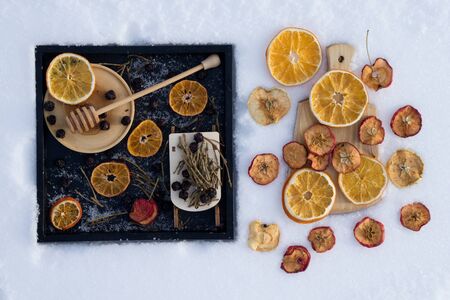 Merry Christmas and  New Year greeting card with dry orange, Clementines tangerines, honey with wooden spoon, toy sled with herbal tea and black berry on black tray  and wooden board  on snow as backgroundの写真素材