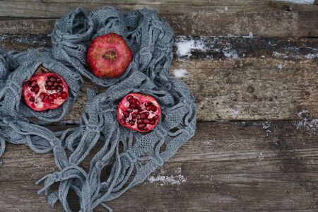Fresh red  pomegranate in gray scarf on wooden old table   as Christmas decorの写真素材