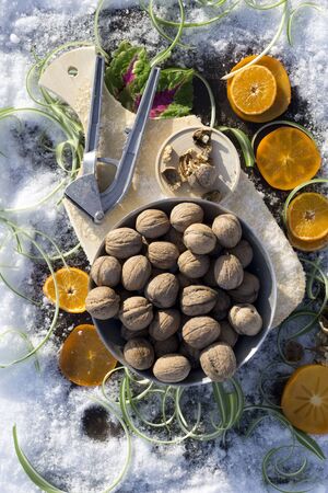 flat lay with  walnut on wooden board,   cracked nut with nutshell, Nutcracker, ebony, mandarin green grass on background with snowの写真素材