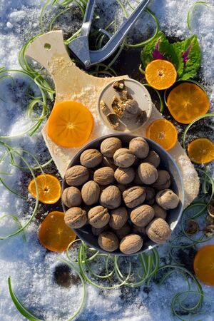 flat lay with  walnut on wooden board,   cracked nut with nutshell, Nutcracker, ebony, mandarin green grass on background with snowの写真素材