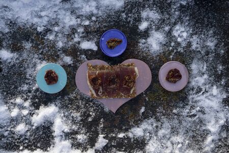A pink heart  with  Traditional  tapas    with  spanish cured meat and  bread chips with seed and  wooden  colors  plate  on background with snowの写真素材