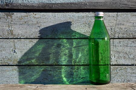 Empty green   bottle against wooden blue old wall on wooden table  under the natural light of the sun,  the big  shade falls on the  wallの写真素材