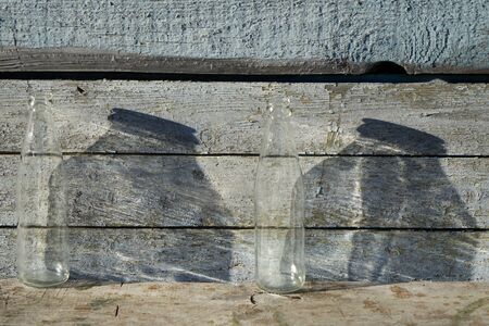 Empty transparent two  bottle against wooden blue old wall on wooden table  under the natural light of the sun,  the big  shade falls on the  wallの写真素材