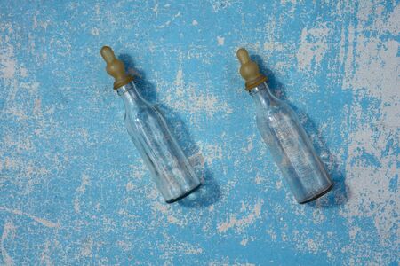 Empty transparent baby bottle for  feeding newborn babies with shadow  on  blue pastel colors  wooden  background under the natural light of the sun. Flat lay. Creative copyspace.の写真素材