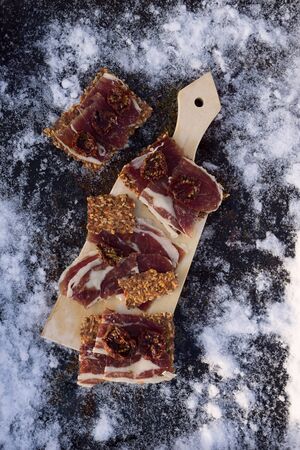 A cutting board  with  Traditional  tapas    with  spanish cured meat, bread chips with seed, sun dried tomato on background with snowの写真素材