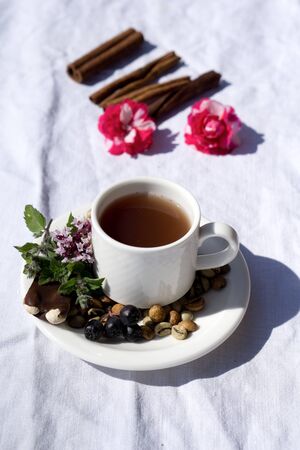 Coffee composition  with  white cup    of coffe with herb  and beans of coffe,  Chocolate,  berry, mint, flower on  linen tableclothtable as backgroundの写真素材