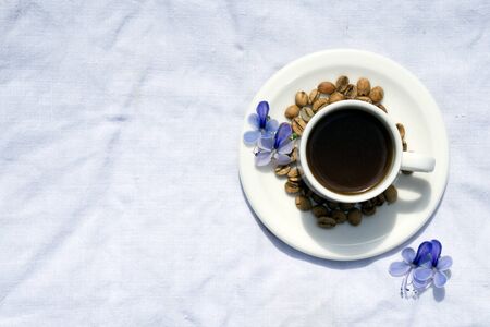 Flat lay Coffee composition  with  white cup  and beans of coffe and blue flower  on  linen tableclothtable as backgroundの写真素材