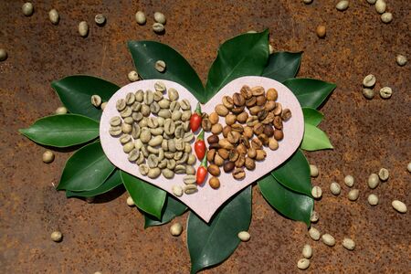 Flat lay  with wooden  pink heart  with green and middle coffee bean on green leaf against textured rustic iron  backgroundの写真素材